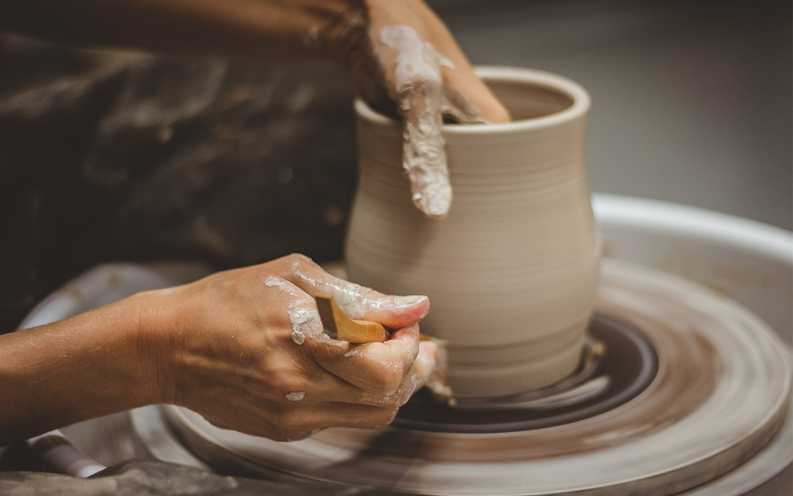 Potter hand making bowl while using pottery tools to shape