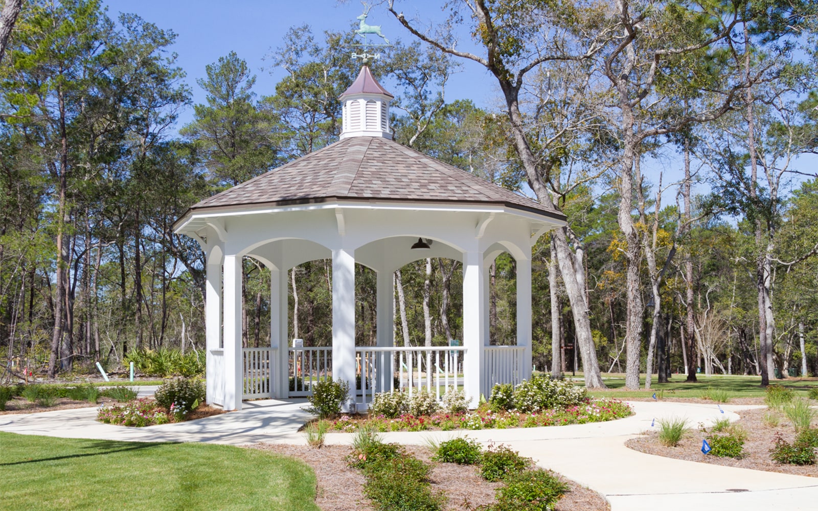 White gazebo sits in the middle of trees and gardens