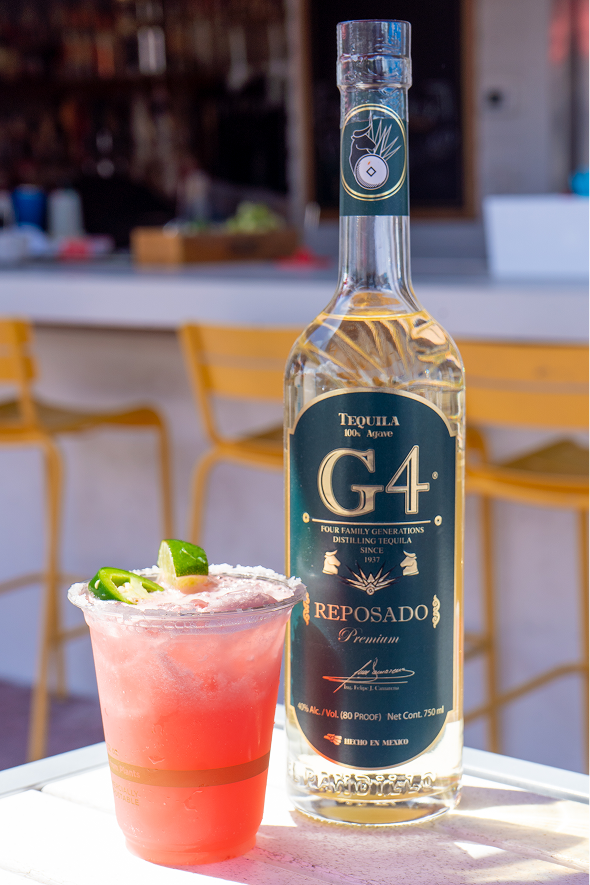 Glass of pink juice next to a g4 margarita bottle